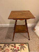 Front view of wooden side table showing square top, turned legs, and lower shelf.
