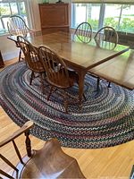 Table partially expanded with chairs around on oval braided rug under window