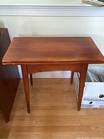 Front view of closed wood table showing rectangular, flat warm brown top with some edge wear and straight tapered legs.