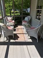 Screened porch view showing four white wicker chairs arranged around two wicker tables; each chair has a pink seat cushion; tables have glass tops.