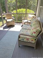 Screened porch view showing tan wicker sofa and two armchairs with floral cushions