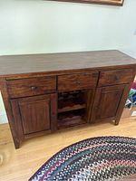 Front view of dark wood wine buffet cabinet showing top, three drawers, two doors, and central wine rack