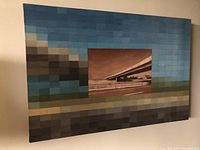 Angled view of the oil painting showing the highway overpass image centered with pixelated blue and green blocks around the edge.