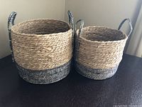 Pair of two-tone woven baskets side by side on a dark surface, showing size difference and dual-tone coloration.