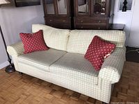 Front view of plaid upholstered couch with two red throw pillows, showing overall condition and design.
