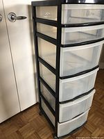 Side view of plastic storage unit with clear drawers and black frame, showing multiple drawers and wheels.