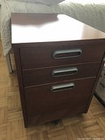 Front view of IKEA wood finish desk drawer unit showing three drawers with metal handles on casters