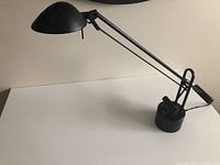 Black desk lamp with articulated arm, dome-shaped shade, and round base shown on a white surface.