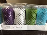 Front view of the set of eight glass tumblers in box showing all colors and circle cut-out pattern