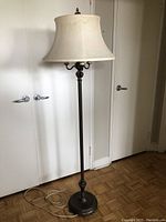Floor lamp fully assembled with fabric shade on top, dark metal base and stand visible in room with white walls and hardwood floors.