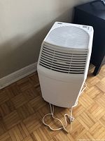 Front view of white Aircare humidifier showing top and front slatted vents with power cord on floor.
