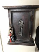 Front closed view of wooden key holder box showing the decorative key motif on the door and the water-damaged top.
