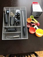 Full view of kitchen essentials including organizer with utensils, colorful measuring cups, and box grater on table.