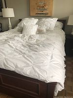 Side angle view of queen wooden bed frame with white bedding and pillows, showing paneled footboard and part of headboard.