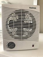 Front view of white Holmes space heater showing grille, control knob, and power light.