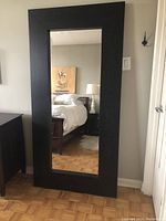 Front view of the large standing mirror showing the black frame and reflection of bedroom