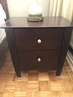 Front view of one dark brown wood bedside table showing 2 drawers with round metal knobs.