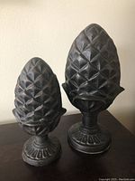 Photo showing front view of two solid pineapple statues, highlighting their textured diamond surfaces and pedestal bases.