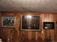 All three framed paintings displayed on paneling wall