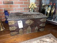 Front view of the dark wood carved chest showing metal corner accents and riveted metal plates.
