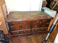 Photo showing entire wood chest with metal detailing on top and sides, drawers, and latch.