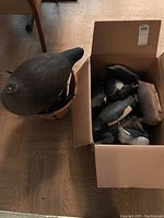 Photo showing large dark molded goose decoy beside a box filled with smaller decoys