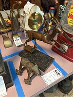 Shows the brass antelope figurine on marble base in mid-leap, with the metal ox figurine on wheels and another small animal figurine visible on the table.