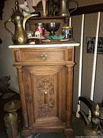 Front view of wooden foyer cabinet showcasing marble top, drawer, and decorative carved door with brass handles.