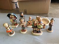 Group photo of seven Hummel figurines and one ashtray, showing the variety and style of the lot.
