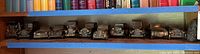 Overview photo showing the full row of nine Banthrico metal car banks in vintage styles and bronze finish on a wooden shelf.