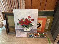 Overall lot showing multiple paintings including floral still life, abstract and landscape art with a colorful street scene painting in front.
