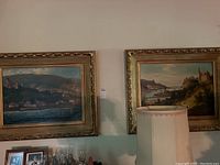 Both paintings hanging side by side above a console with glassware