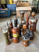 Overall view of 13 wooden pepper mills arranged on the floor showing various shapes and finishes