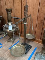 Full view of the brass balance scales with marble base standing on wooden floor against wood paneling.