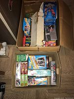 Top image showing two cardboard boxes filled with assorted trading card boxes and unopened packs, including visible Topps basketball and football cards.