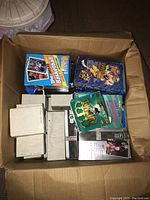 Box containing various unopened and opened basketball and football trading card boxes and packs.