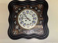 Front view of square wall clock with black wavy frame, wood inlay, and ceramic Roman numeral digits on clock face.