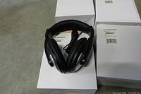 Photo showing one black Synchrotech over ear stereo headphone with padded headband and ear cushions, cable coiled in middle, displayed on white boxes.