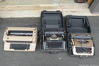 Front view of three vintage electric typewriters with cases open, showing keyboards and platen rollers