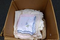 Box containing assorted lace and crochet napkins and placemats including embroidered and scalloped edge cloths