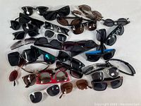 Photo showing an assortment of 30 sunglasses spread out, displaying multiple styles including rectangular, cat-eye, and wrap-around with mixed colors and lens types.