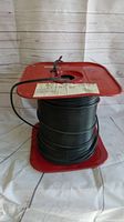 Black precision video cable wire wound on a red metal spool with a label attached, shown from one side
