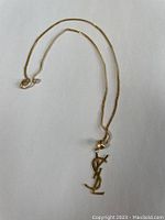 Full view of gold chain with YSL pendant on white background