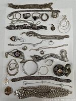 Photo showing assorted silver jewelry laid out on white background with chains, rings, bracelets and earrings.