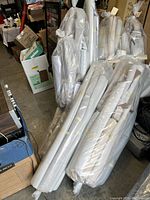 Photo showing multiple large rolls of auto upholstery material wrapped in plastic, rolled and stacked vertically and horizontally.