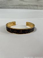 Side view of gold tone bangle bracelet with LV monogram canvas inlay on top, curved open cuff style.