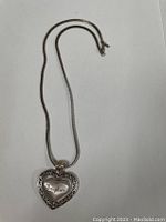 Silver necklace with heart pendant showing engraving 'Daughter' and decorative outer border.