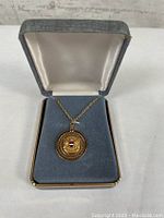 United Airlines pendant on gold necklace chain displayed inside open grey jewelry box with padded white interior.
