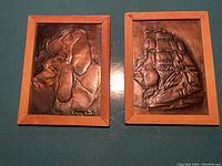 Photo showing two framed brass etchings on a flat surface; one with dog and bird design, the other with sailing ship design