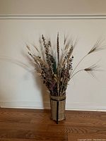 Front view of the tall wicker basket containing dried floral arrangement against white wall on hardwood floor